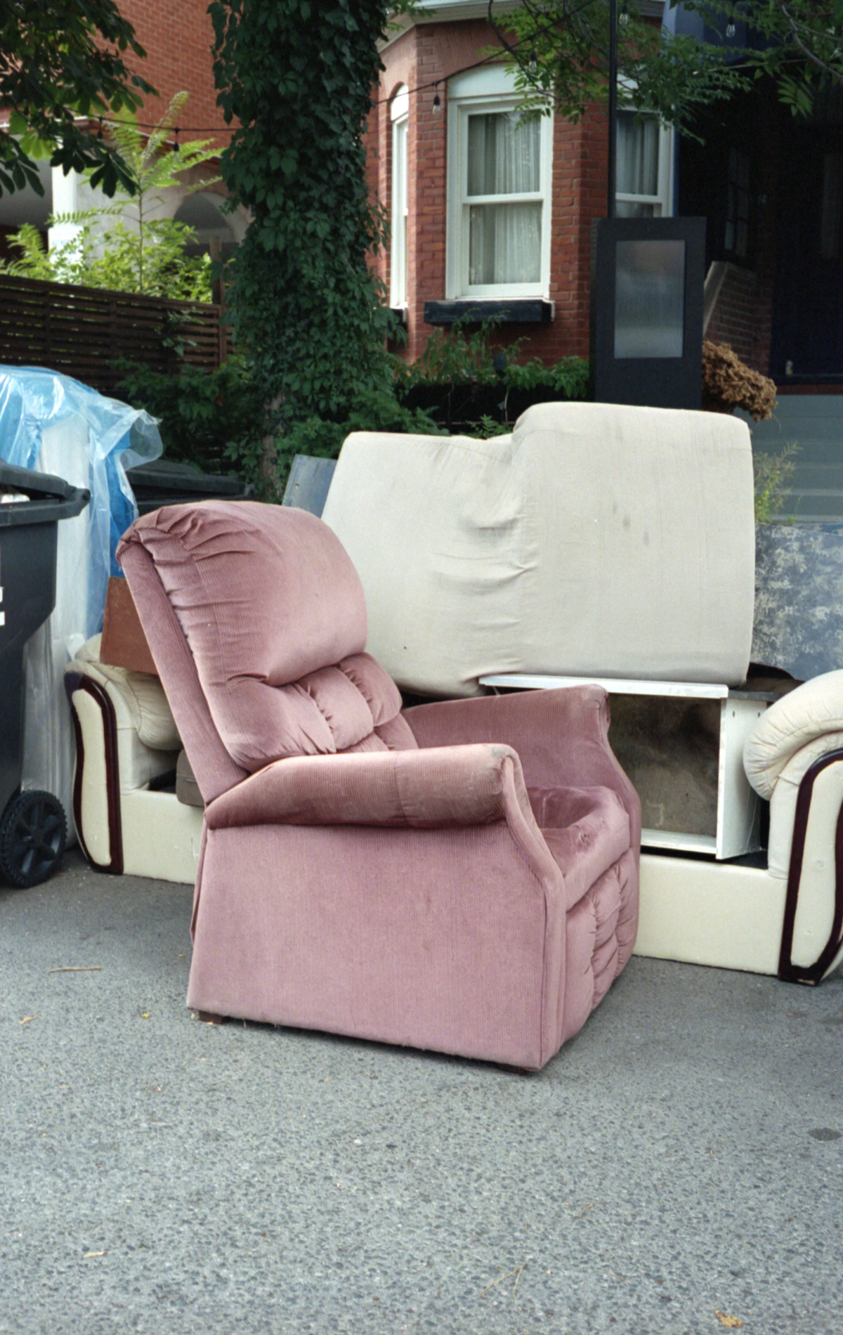 A worn recliner and sofa set curbside in front of a house for furniture removal