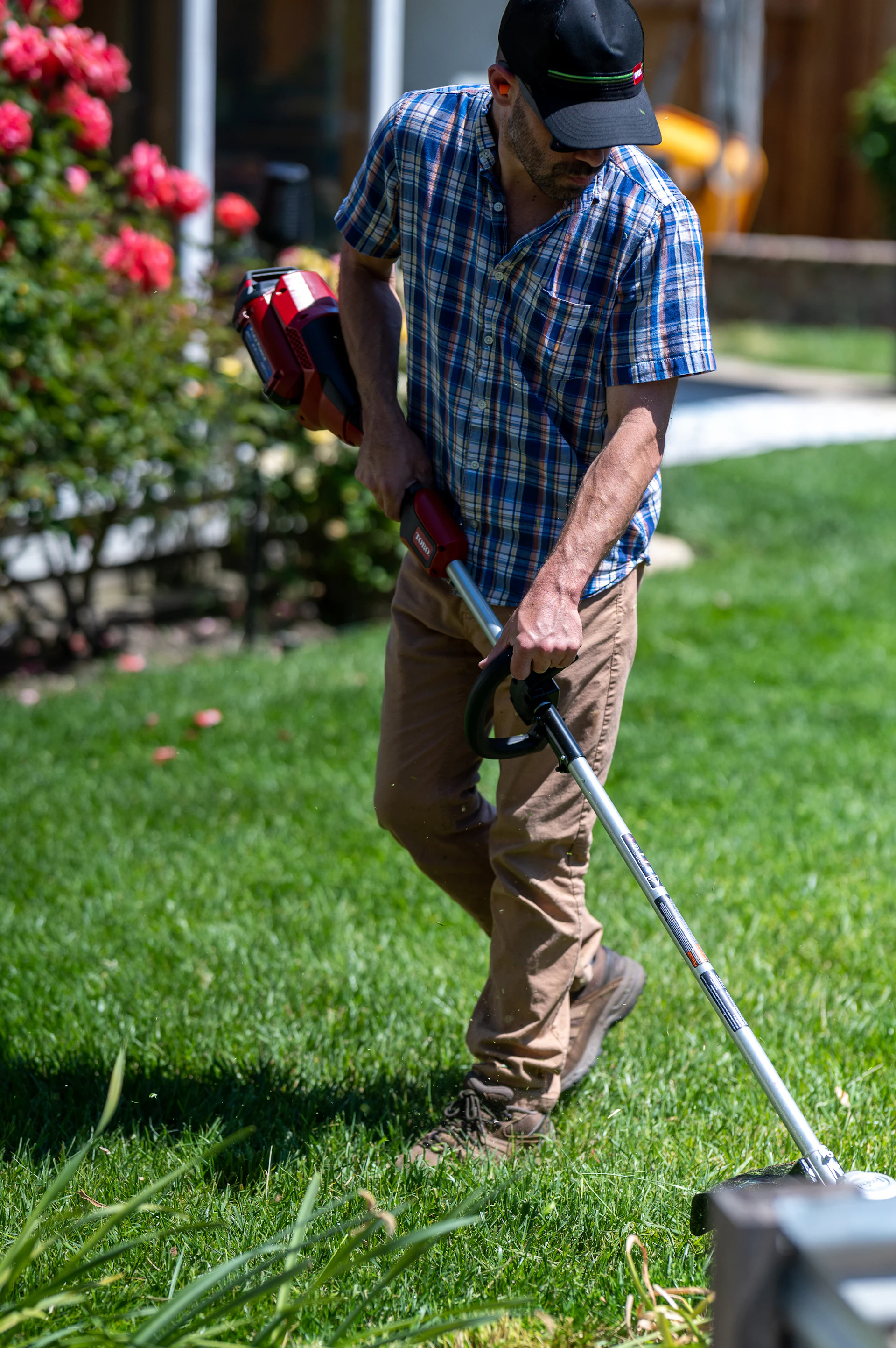 A lawn care technician trimming the grass edge along a flower bed on a sunny residential property
